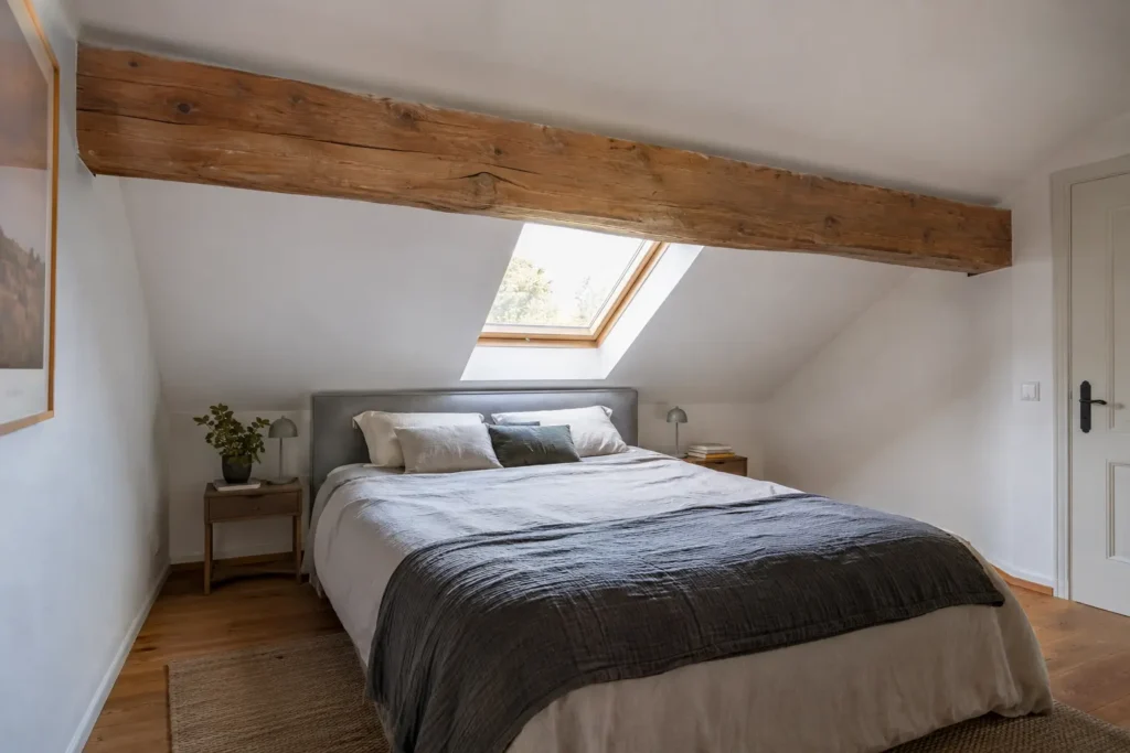 Schlafzimmer unter einer Dachschräge mit kantigem Holzbalken quer über dem Bett